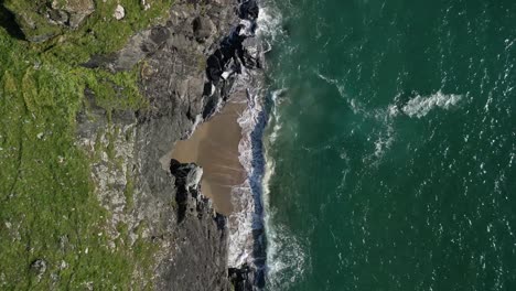 cornish beach cove with ocean waves crashing against the rocks from a top down descending drone shot, cornwall, uk