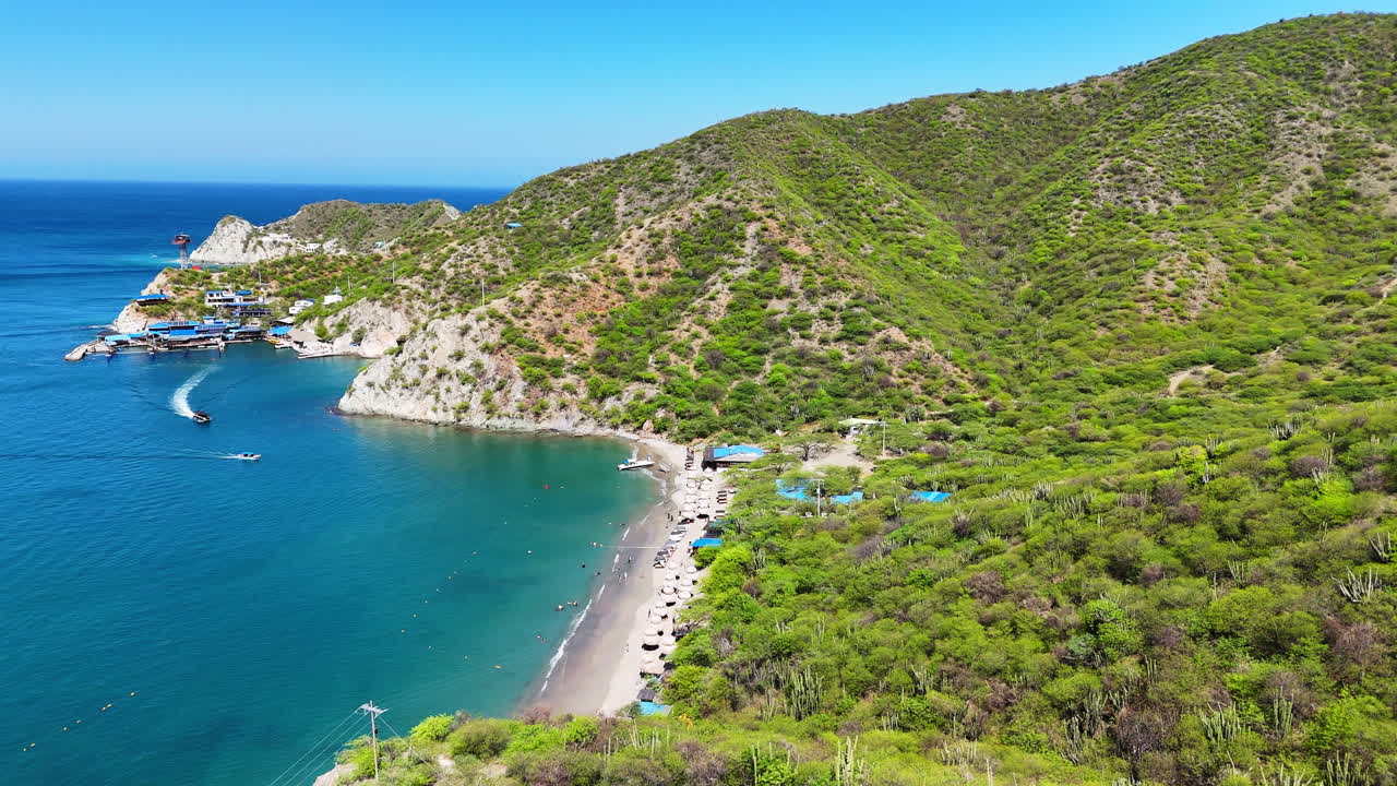 Pohled dronu na pláž Playa Inca Inca v Santa Martě. Odlehlá tropická zátoka s přírodními úkryty a zelenými horami, zatímco se lodě blíží k tyrkysovému pobřeží. Pobřežní krajina v Kolumbii. Filmové.