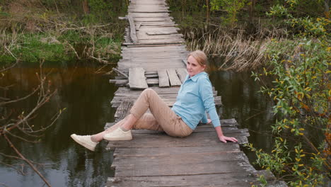 woman sitting on old wooden bridge over a river