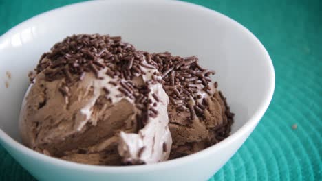 female hand with red nails dropping chocolate sprinkles on top of three ice cream balls inside a white bowl