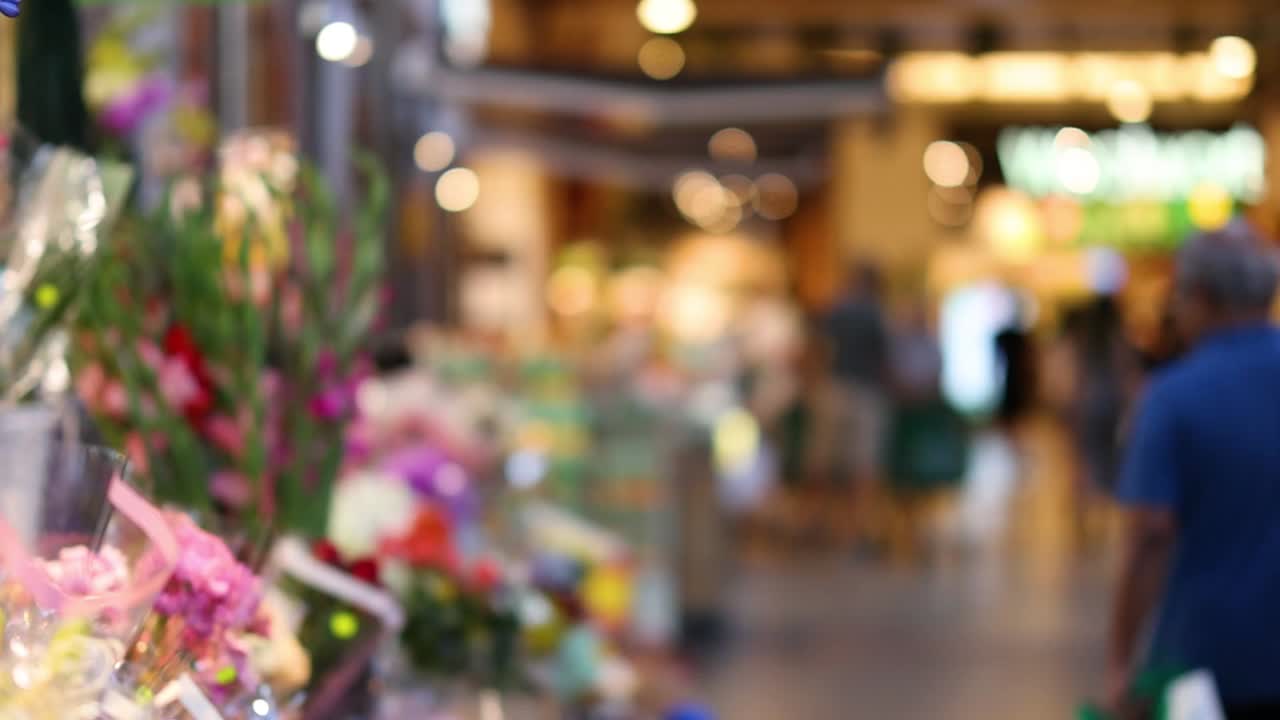 Vibrant flower arrangements line the walkway as people stroll through the bustling market area.