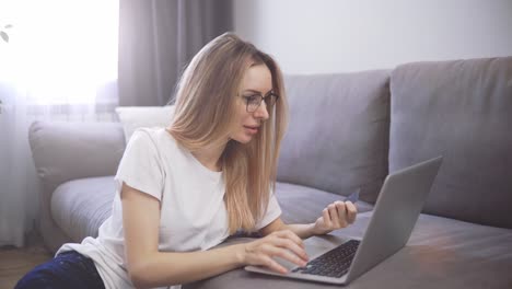 Blonde-woman-sitting-on-the-floor,-pays-for-purchases-online-with-a-credit-card-and-laptop