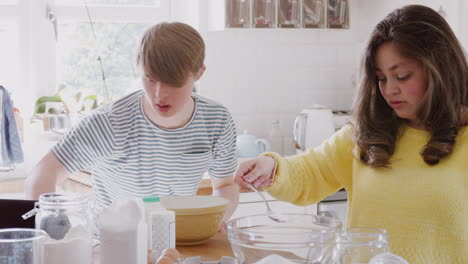 Young-Downs-Syndrome-Couple-Following-Recipe-On-Digital-Tablet-To-Bake-Cake-In-Kitchen-At-Home