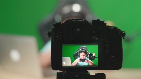 camera display of excited asian little boy playing video game with mobile phone while live stream on green screen