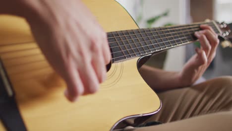 close up biracial man sitting on sofa in living room playing guitar