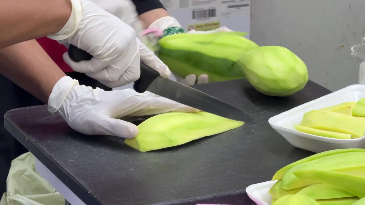 キッチンで新鮮な青パパイヤの皮をむき、スライスする作業員たち