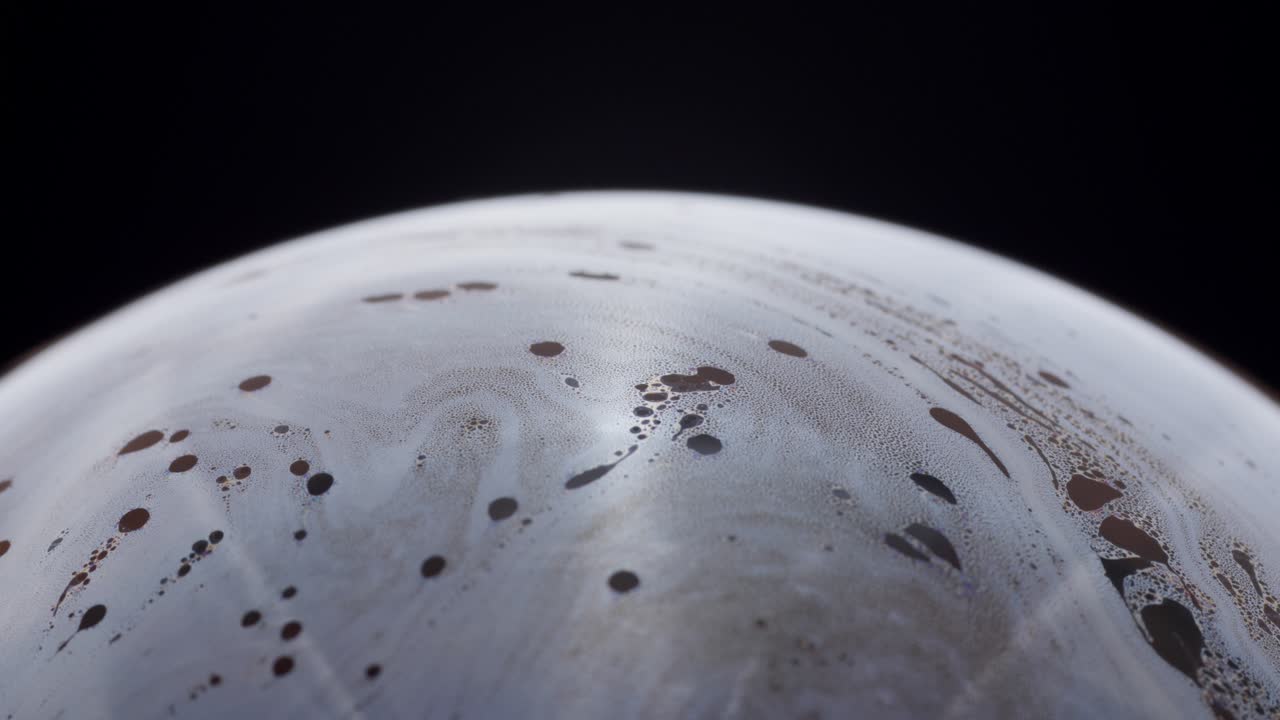 los intrincados patrones dentro de una burbuja de jabón crean la ilusión de un planeta lejano contra un vacío oscuro.