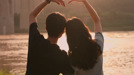 silhouette of romantic couple's back in love doing picnic standing on the shore comparing hearts, background for valentine's day at sunset