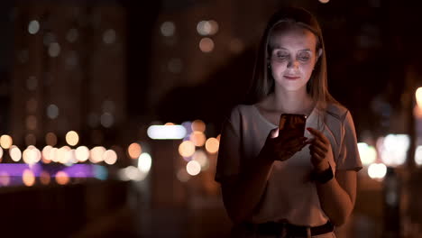 young woman tourist travels through the night megalopolis and writes text messages on social networks about the journey holds the phone in her hands and looks at the screen of the gadget