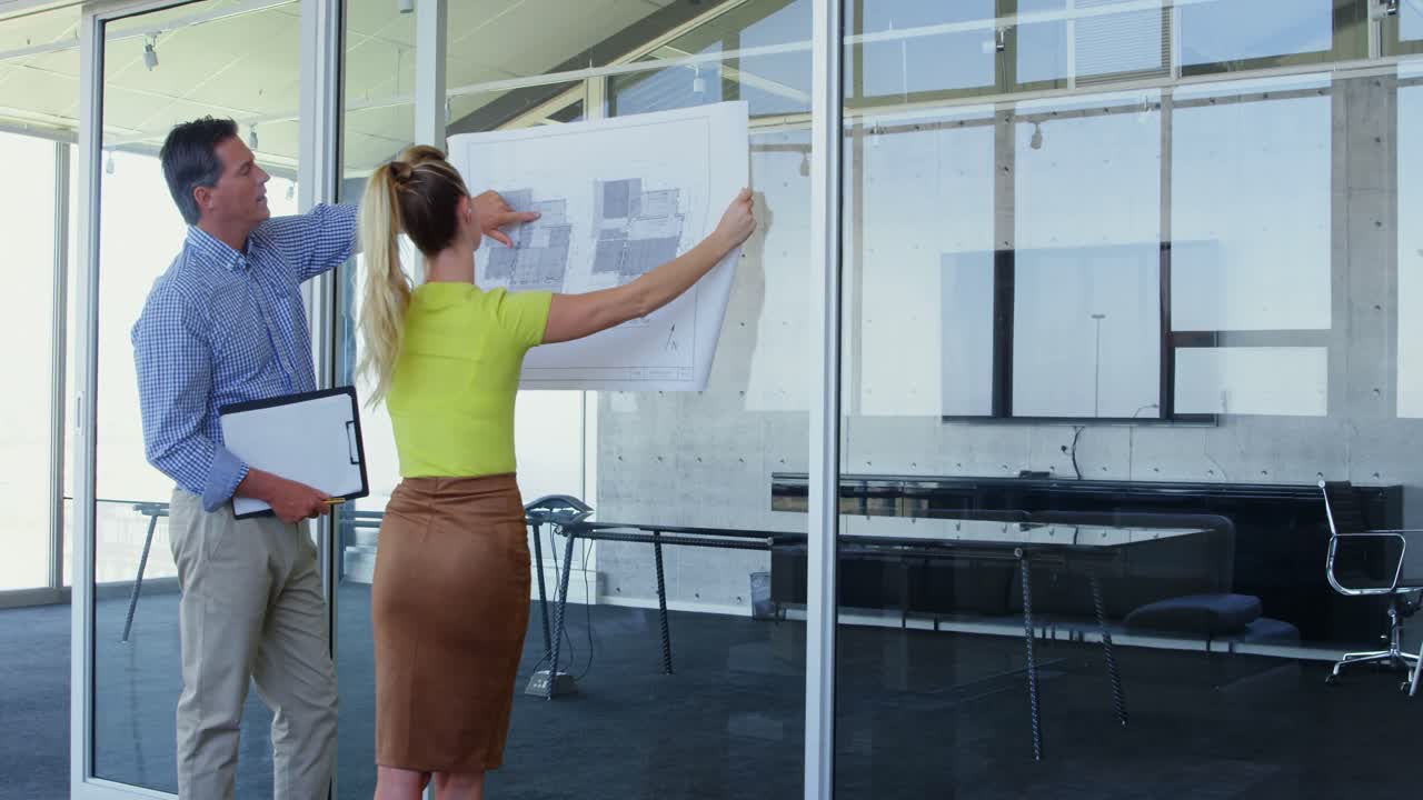 Caucasian male and female architects discussing over blueprint in the office 4k