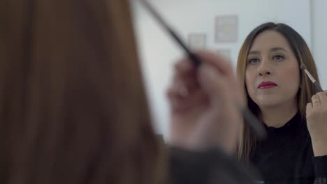 Woman-with-brown-hair-applying-make-up-powder-to-cheeks-and-bridge-of-nose-using-a-large-mirror