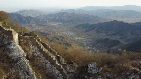 Tourist-climbs-steep-broken-stairs,-Great-wall-of-China,-town-below