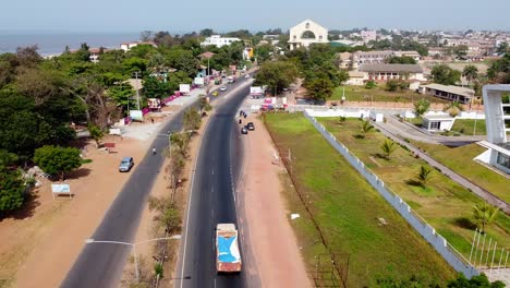 Luftaufnahme-Des-Stadteingangs-Von-Banjul-In-Der-Nähe-Des-Arch-22-Denkmals,-Des-Triumphbogens-Der-Stadt-Mit-Blick-Auf-Die-Stark-Befahrene-Straße-Mit-Verkehr-Und-Gebäuden-An-Einem-Sonnigen-Tag