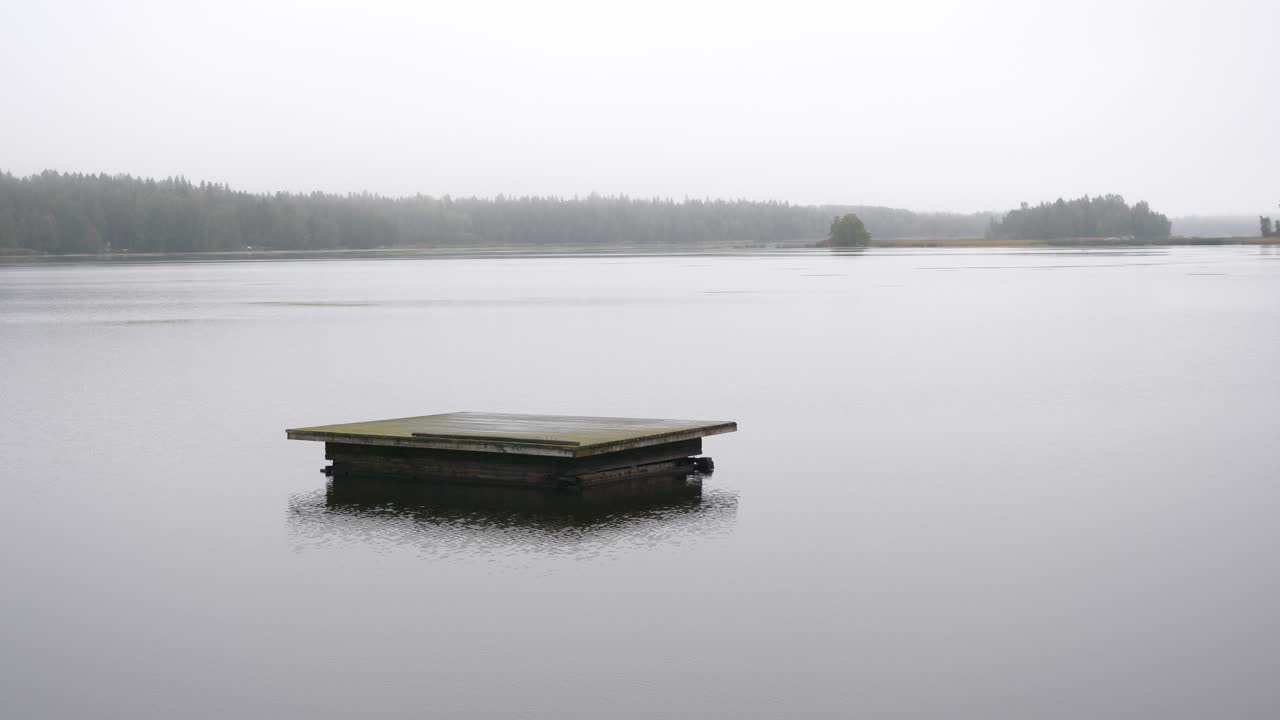 Unhappy depression concept, rain falling on isolated swimming platform in dull gray weather, cottage country landscape