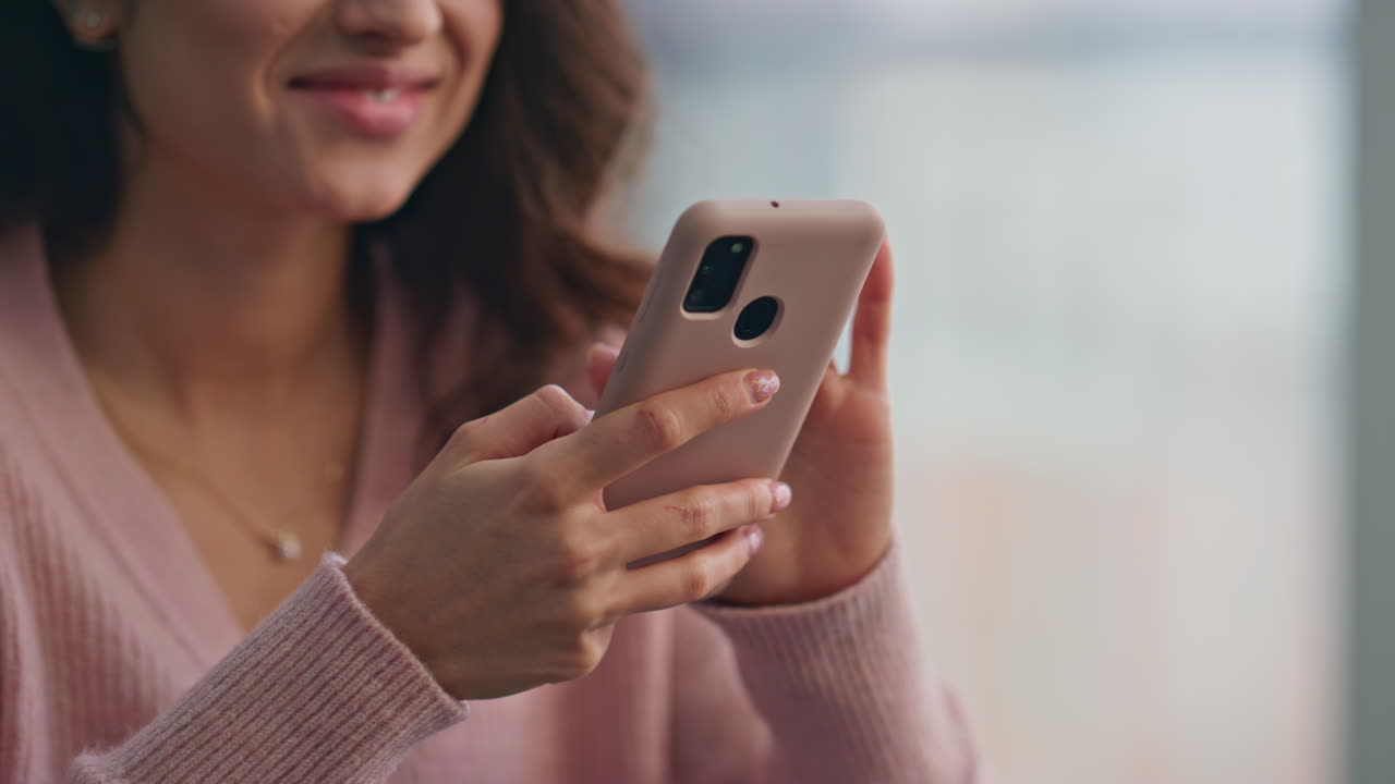Primo piano di ragazza sorridente che digita sul cellulare a casa. Donna felice che invia messaggi.