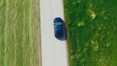 topshot of a blue bmw car driving through countryside, surrounded by green meadows in breathtaking drone footage