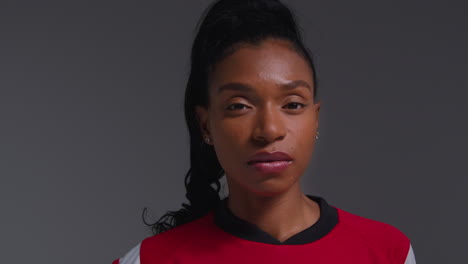 Close-Up-Studio-Portrait-Of-Serious-Female-Football-Or-Soccer-Player-Wearing-Team-Shirt-Shot-Against-Grey-Background