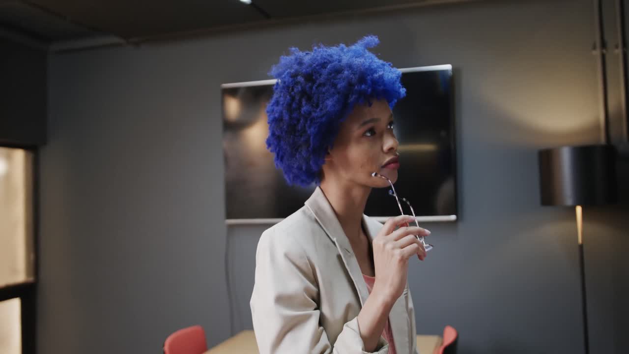 회의실에서 파란색 아프로를 들고 안경을 들고 있는 행복한 두 인종의 사업가 여성의 초상화, 느린 동작