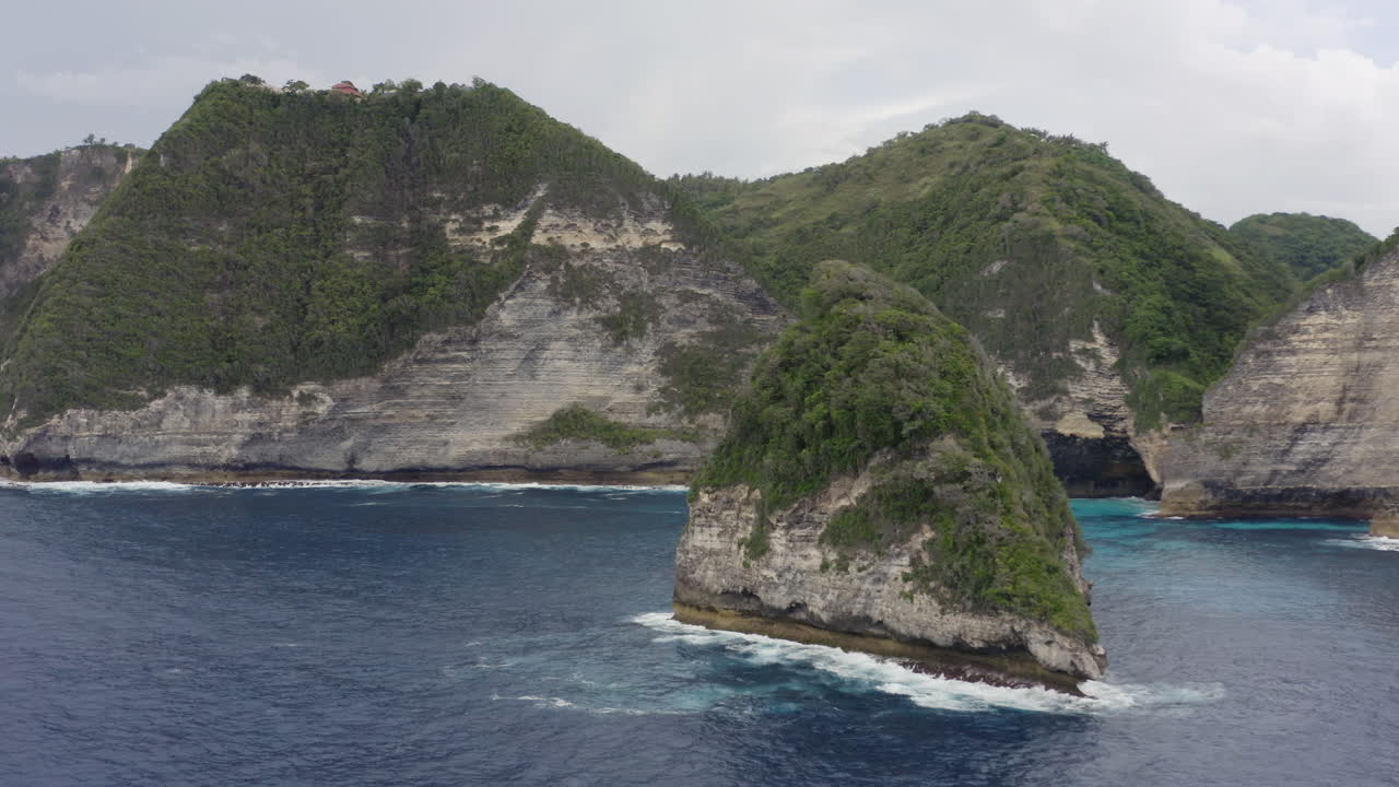 Coast line of Nusa Penida with huge cliffs , islands and green vegetation on top and ocean waves crushing ashore, Bali, Indonesia. Aerial shot.
