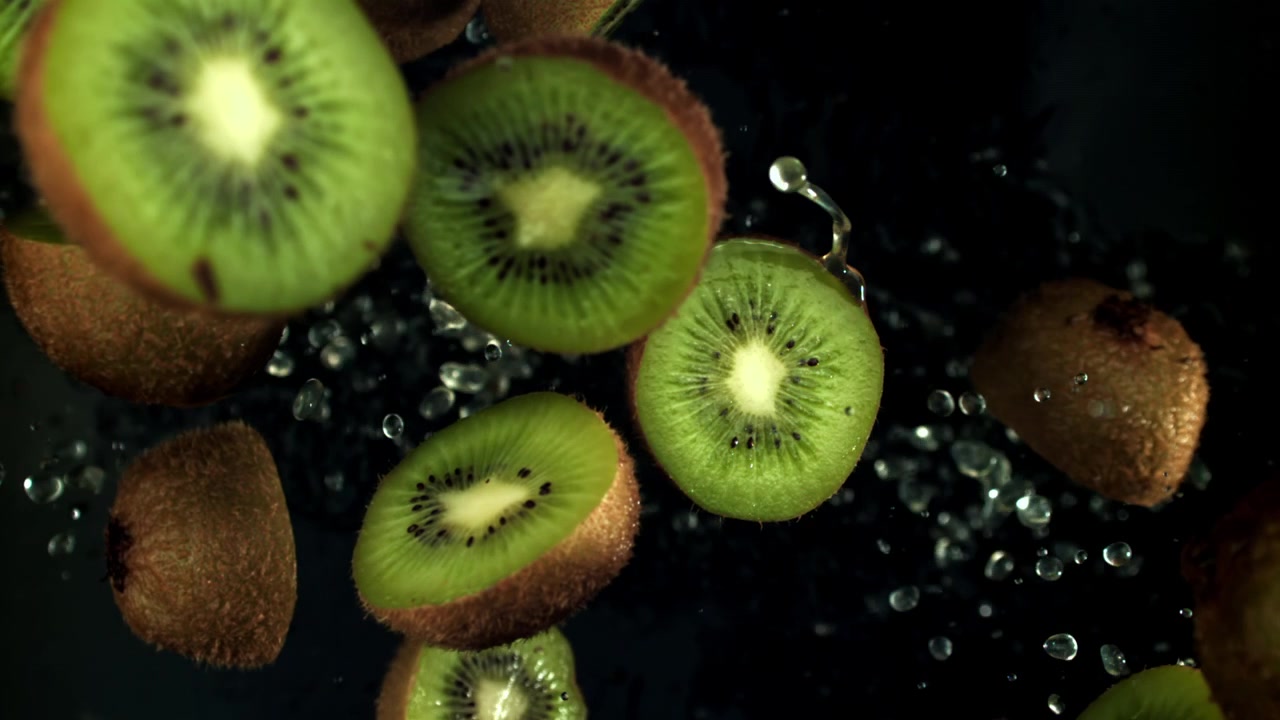 Mitades de kiwi fresco cayendo en el agua en cámara lenta