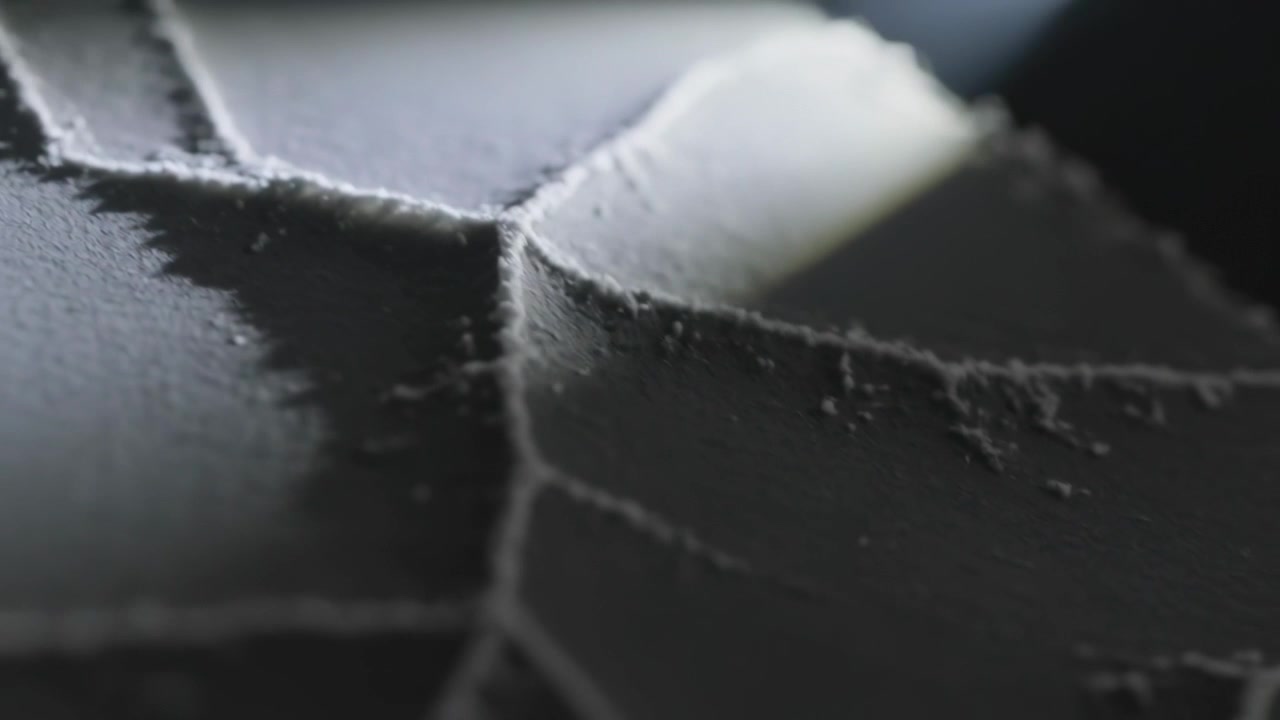 Telecamera che si allontana rivelando una superficie stratificata e crepata con bordi strappati per la texture, e detriti di polvere.