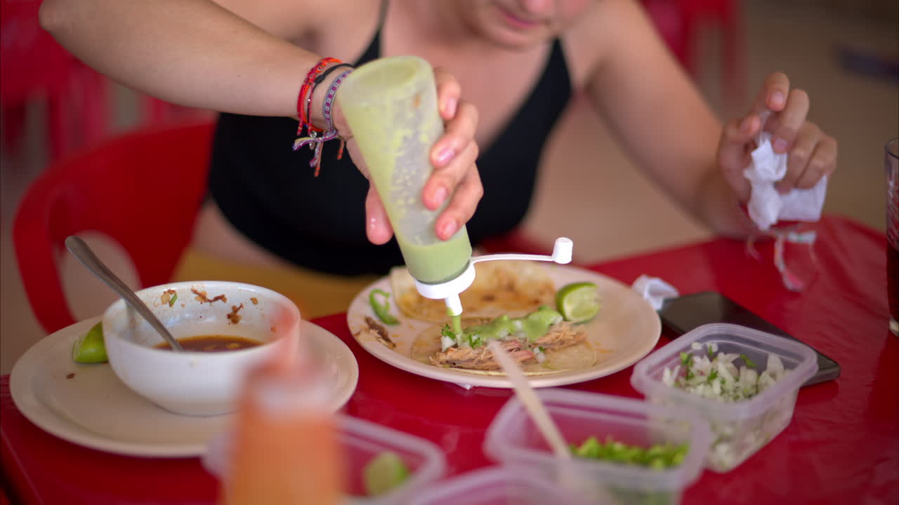 cierre en cámara lenta de una mujer latina preparando su taco de barbacoa con salsa de chile verde en un restaurante en méxico