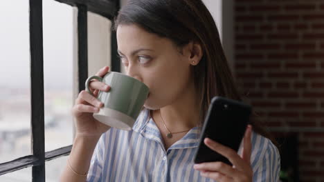 beautiful hispanic woman drinking coffee at home using smartphone enjoying relaxed morning browsing messages looking out window planning ahead texting on mobile phone networking