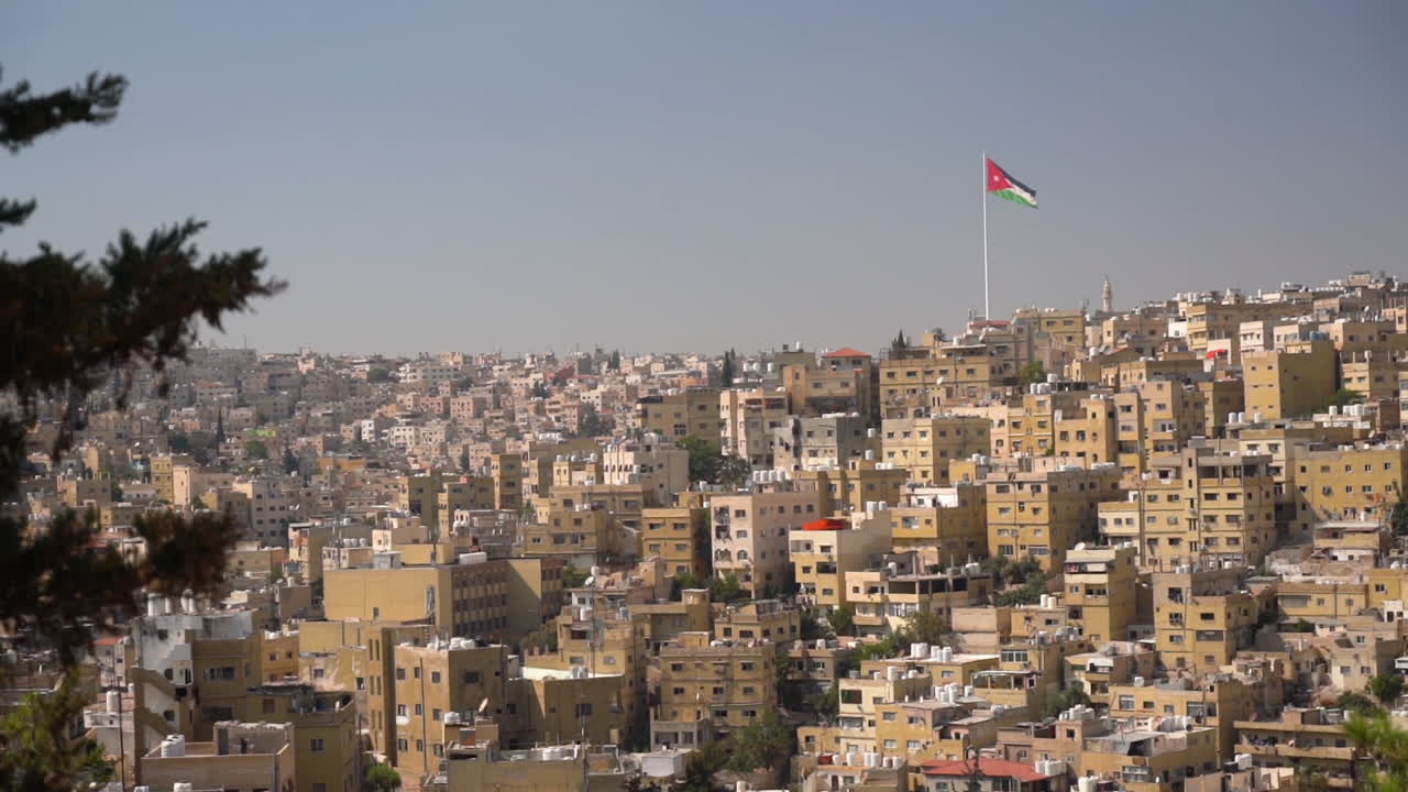bandera jordana ondeando en la cima de una colina sobre el barrio residencial de la ladera, amman, jordania el día soleado