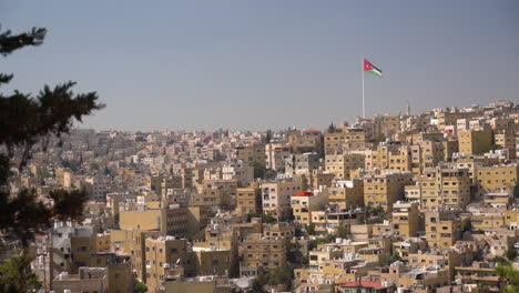 jordanian flag waving on hilltop above hillside residential neighborhood, amman, jordan on suny day