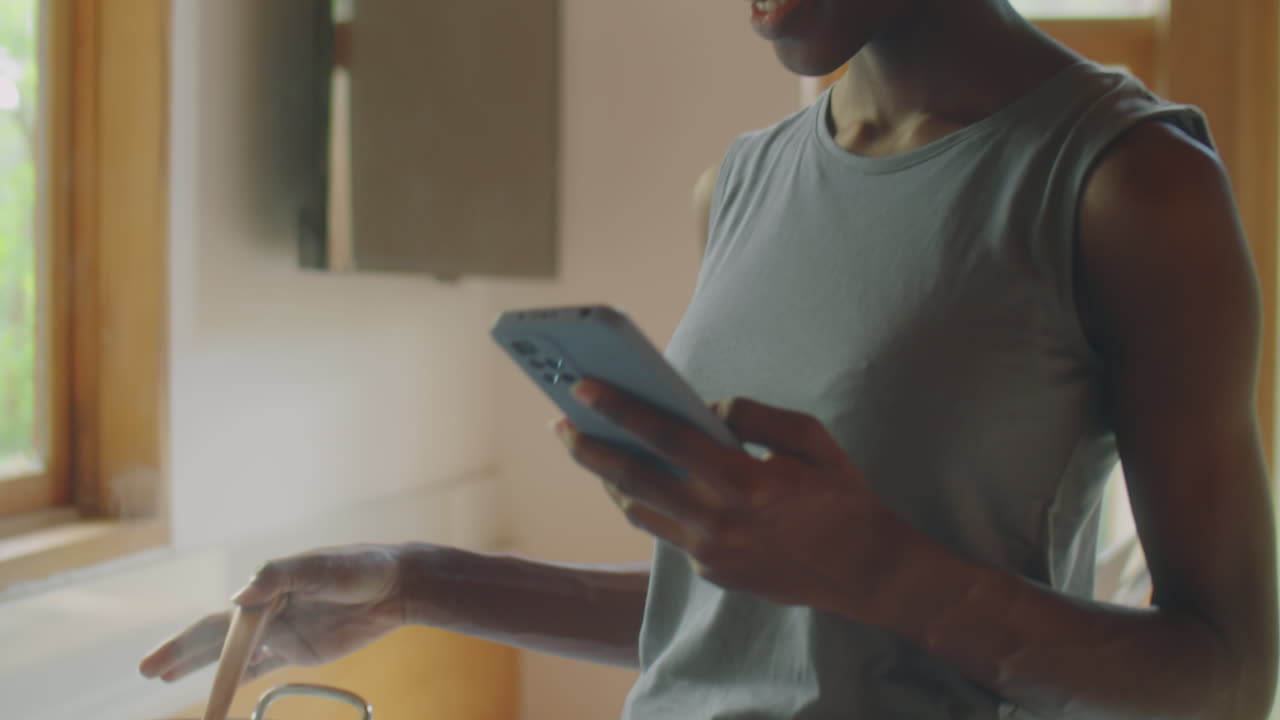 Black Woman Using Phone and Smiling while Cooking Meal