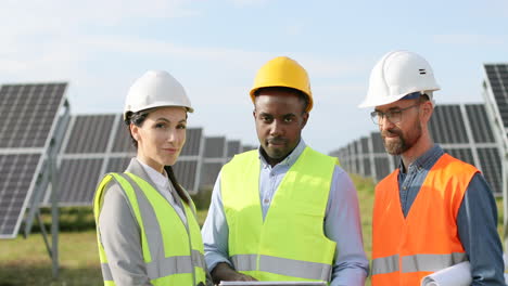 –°amera haciendo zoom en tres técnicos solares agrícolas multiétnicos que miran el portapapeles en una plantación solar