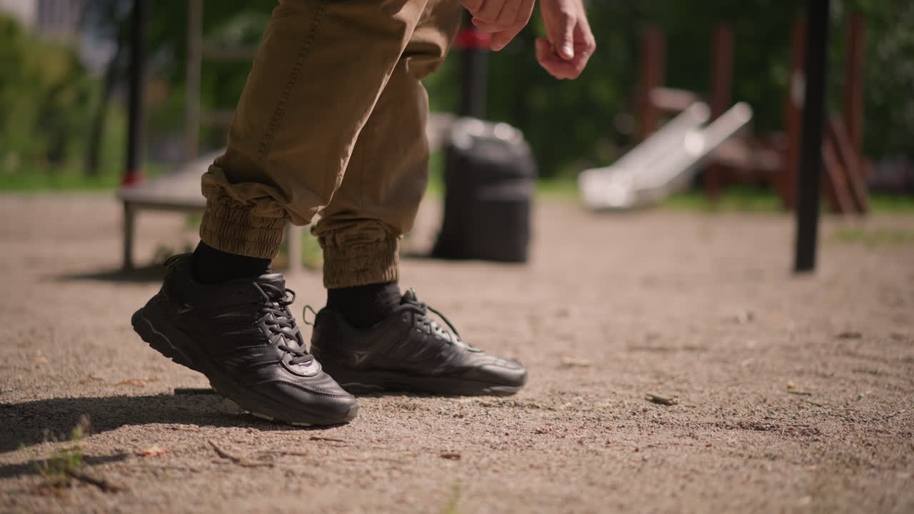 Closeup Of Man Adjusting Footwear Outdoors, Man Carefully Tests His Boots On Rugged Gravel Surface, Closeup View Of Man In Fitness Park Adjusting Boots And Checking Ground Stability
