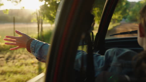mujer en el coche con la mano afuera de la ventana sintiendo el viento soplando a través de los dedos conduciendo en el campo viajando en vacaciones de verano viaje por carretera disfrutando de la libertad en la carretera al atardecer