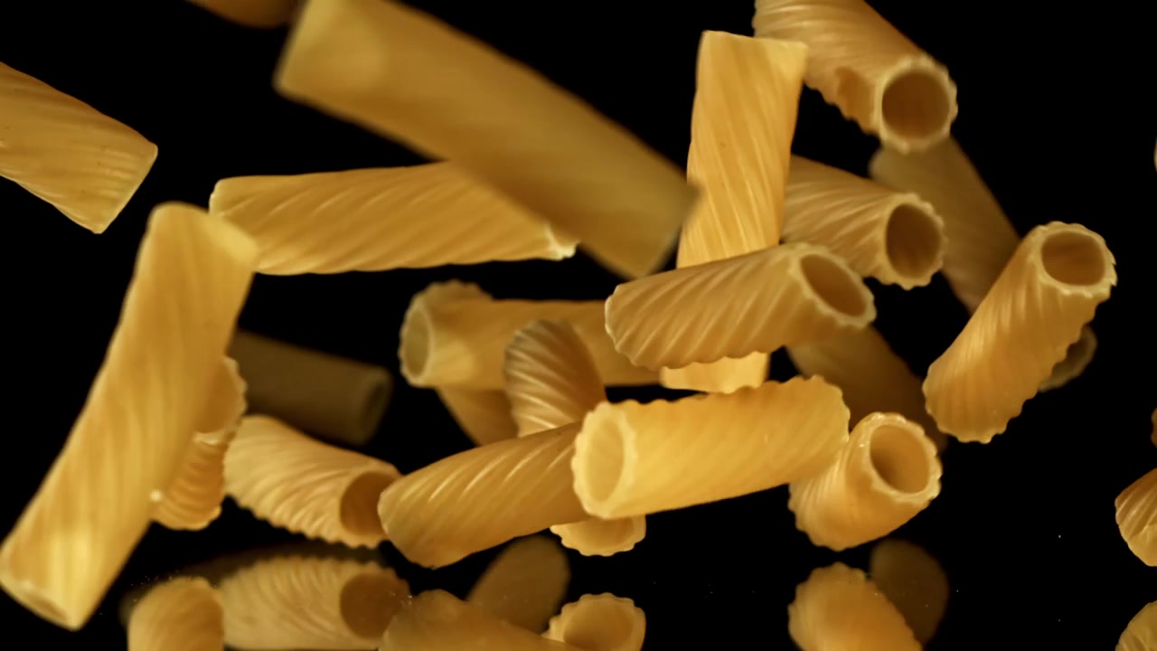 Pasta maccheroni secca che cade al rallentatore su sfondo nero.
