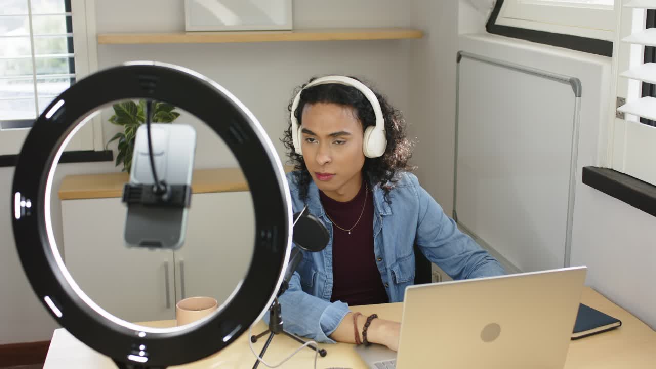 Streamer no binario encendiendo una luz anular, escribiendo en un portátil y hablando por un micrófono para una transmisión de estudio