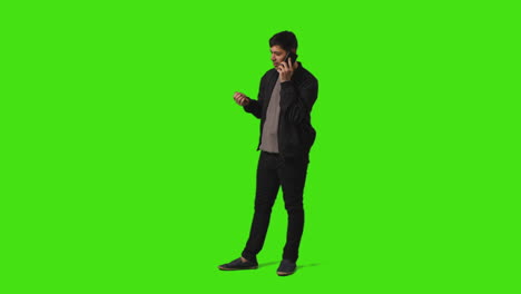 Smiling-Young-Man-Talking-On-Mobile-Phone-Standing-Against-Green-Screen-Studio-Background