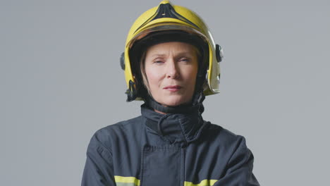 studio portrait of serious mature female firefighter wearing helmet against plain background