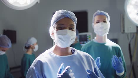 video of smiling biracial female surgeon and diverse colleague in face masks in operating theatre