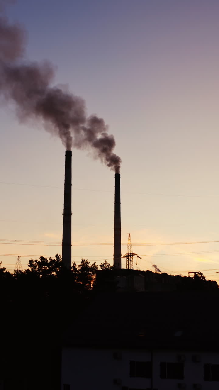 Industrial pipes of the thermal power plant at sunset. Smoke from the factory chimneys against the evening sky. The concept of environmental pollution. Vertical video