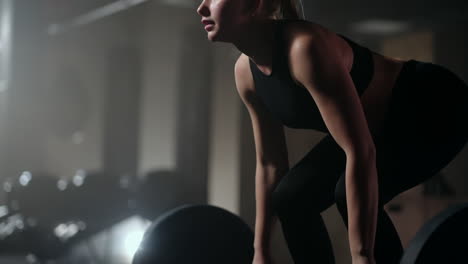 slow motion: a woman lifts a barbell in a dark gym with a lot of weight. a strong young woman lifts weights for a workout