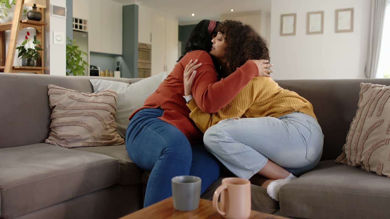 African American mother and daughter hugging on couch at home then offering comforting advice
