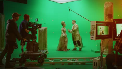 on big film studio professional crew shooting period costume drama movie. on set: director controls cameraman shooting green screen scene with two actors talented wearing renaissance clothes talking