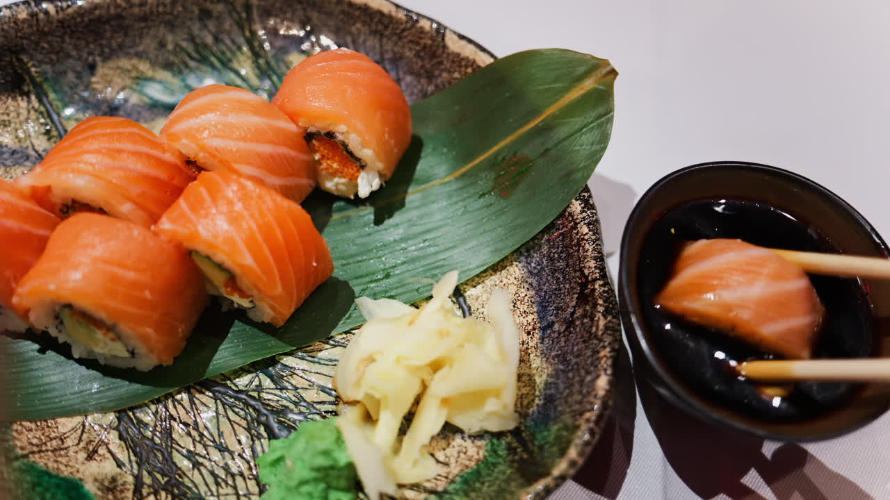 Close up of a woman picking up a Philadelphia sushi roll and dipping it in soy sauce