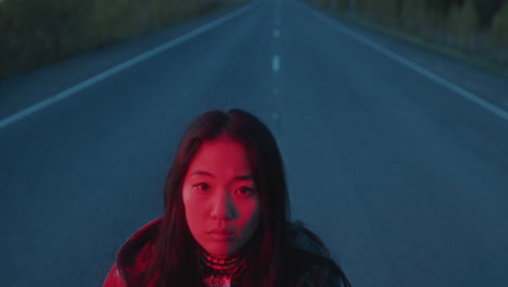 portrait of young woman illuminated by red light on empty road at dusk