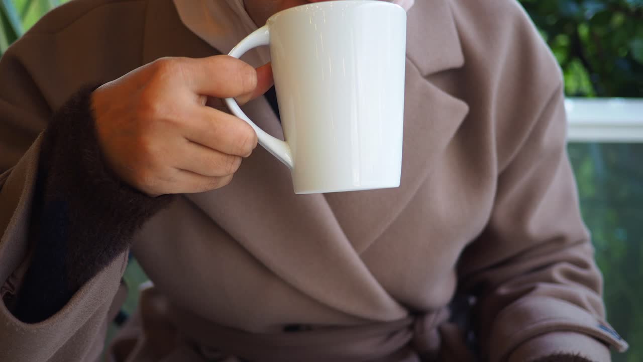 Primo piano di una persona che sorseggia una bevanda calda da una tazza bianca