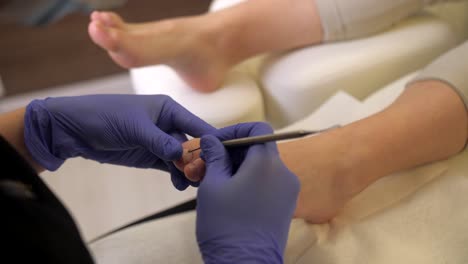 pedicura femenina limpiando la cutícula de otra mujer en el dedo del pie, dentro del detalle del salón de belleza