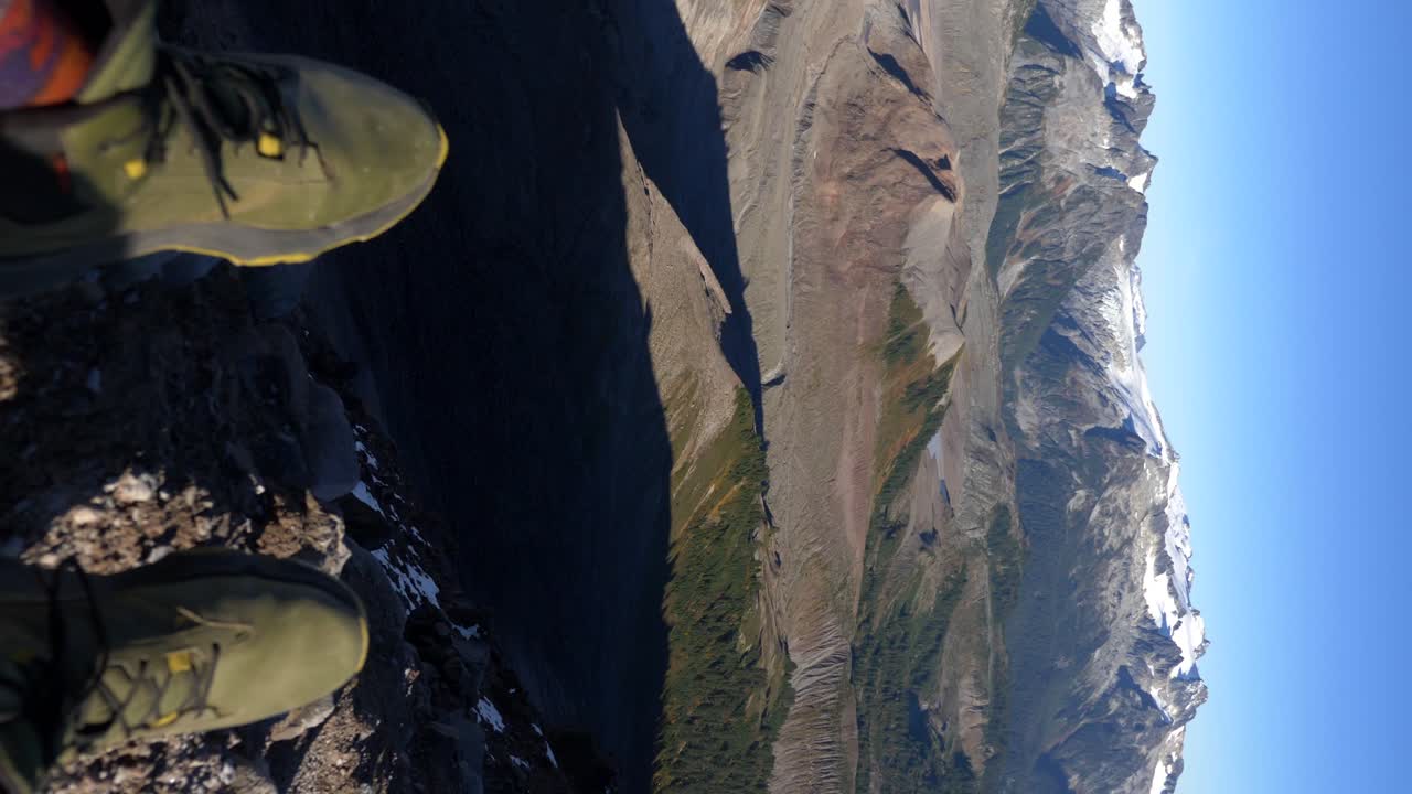 disparo vertical - excursionista sentado en la cima del acantilado mirando las montañas rocosas en la columbia británica, canadá