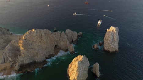Filmische-Drohnenaufnahme-Von-Meeresklippen-Mit-Booten-Im-Wasser-In-Cabo-San-Lucas-Mexiko
