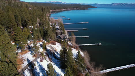 Aerial-View-of-Lake-Tahoe-Wooden-Docks-on-Sunny-Winter-Day,-Calm-Water-and-Pine-Forest