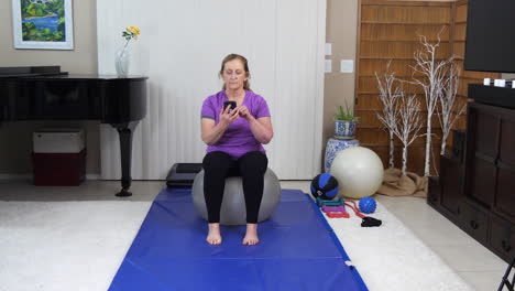 Mujer-Usando-Un-Teléfono-Celular-Mientras-Está-Sentada-Sobre-Una-Pelota-De-Ejercicios-En-Casa,-Con-Estática-Bloqueada